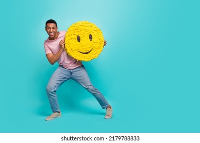 Full length photo of funky sweet man dressed pink t-shirt jumping holding smiley pinata empty space isolated turquoise color background