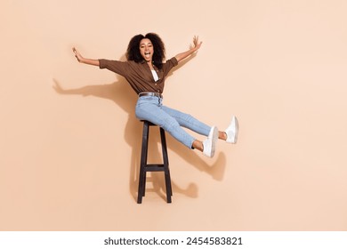 Full length photo of funny carefree girl wear brown blouse jeans sit on stool raising hands falling isolated on pastel color background - Powered by Shutterstock