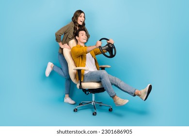 Full length photo of funny couple brother sister play push chair hold steering wheel fast speed driving excited isolated on blue color background