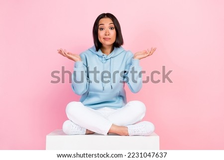 Full length photo of funny doubtful lady wear blue hoodie relaxing white platform comparing arms empty space isolated pink color background