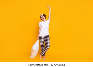 Full Length Photo Of Funny Lady Sleepy Morning Eyes Closed Enjoy Saturday Raise Hands Up Stretching Hold Pillow Wear White T-shirt Plaid Pajama Pants Isolated Yellow Color Background