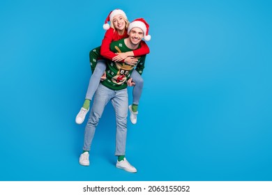 Full length photo of funny millennial couple piggyback wear sweater hat jeans shoes isolated on blue background - Powered by Shutterstock