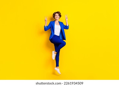 Full length photo of funny pretty lady dressed blue blazer jumping high showing two v-signs isolated yellow color background