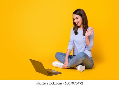 Full Length Photo Of Girl Coach Sit Floor Legs Crossed Use Laptop Video Call Greet Conference Members Wave Hand Wear Purple Violet Sweater Denim Jeans Isolated Yellow Color Background