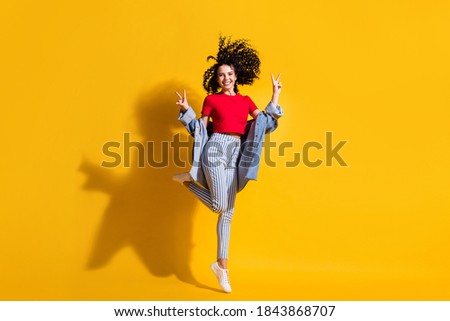 Full length photo of girl stay tiptoe show v-sign wear striped jeans cropped red t-shirt jacket sneakers isolated yellow color background