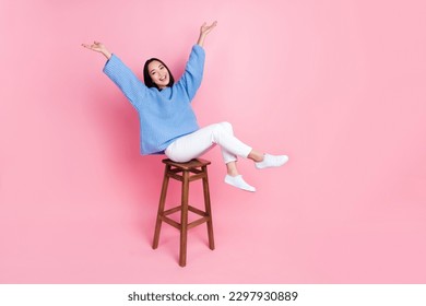 Full length photo of gorgeous pretty girl blue sweater white pants sitting on bar stool raising arms up isolated on pink color background - Shutterstock ID 2297930889