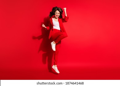 Full length photo of gorgeous young lady jump raise fist wear blazer pants footwear isolated red color background