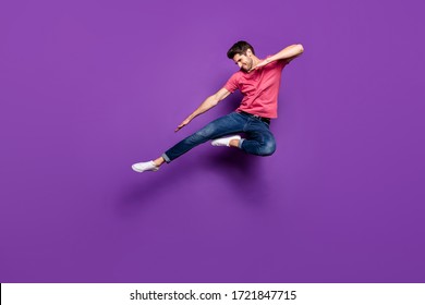 Full length photo of handsome attractive guy jump high up spread arms dance strange dab moves wear casual pink t-shirt jeans footwear isolated purple color background