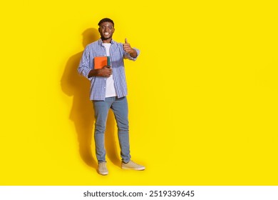 Full length photo of handsome good mood guy wear plaid shirt holding textbooks showing thumb up emtpy space isolated yellow color background - Powered by Shutterstock