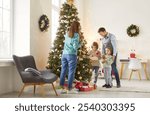 Full length photo of happy family of mother, father and two little children decorating Christmas fir tree together standing in festive living room at home. New Year and winter holidays concept.