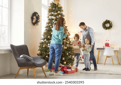 Full length photo of happy family of mother, father and two little children decorating Christmas fir tree together standing in festive living room at home. New Year and winter holidays concept. - Powered by Shutterstock