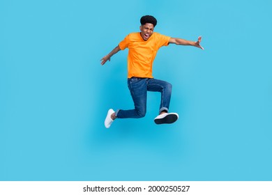 Full length photo of impressed brunet millennial guy jump yell wear orange t-shirt jeans isolated on blue color background - Shutterstock ID 2000250527