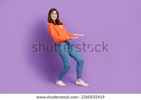 Full length photo of impressed funny woman dressed orange cardigan carrying arms empty space isolated purple color background
