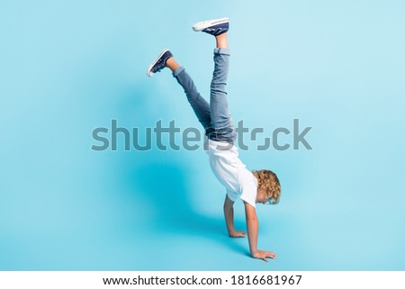 Full length photo of little kid stand hands raise legs wear white shirt jeans sneakers isolated blue color background