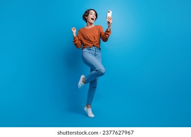 Full length photo of lovely young lady celebrate big discount eshop hold device wear trendy brown garment isolated on blue color background - Powered by Shutterstock