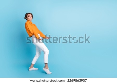 Full length photo of lovely young lady carry hold heavy empty space wear trendy orange clothes isolated on blue color background