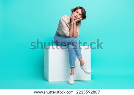 Full length photo of minded lonely lady sit cube look up empty space hand face autumn melancholy bad mood isolated cyan color background