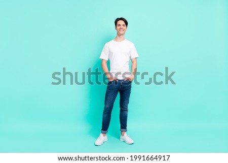 Full length photo of nice brunet hairdo teen guy stand wear t-shirt jeans isolated on teal color background