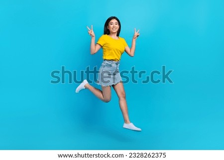 Full length photo of nice cheerful girl good mood dressed yellow t-shirt denim skirt show v-sign flying isolated on blue color background