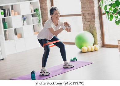 Full length photo of nice pensioner woman resistance band squats sportswear home exercising routine living room healthy lifestyle - Powered by Shutterstock