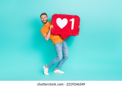 Full Length Photo Of Optimistic Appreciative Guy Brown Beard Wear Orange T-shirt Hold Big Red Like Icon Isolated On Teal Color Background