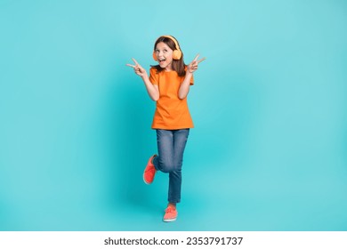 Full length photo of overjoyed positive small girl wear orange stylish clothes hand v-sign epty space ad isolated on cyan color background