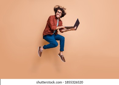 Full length photo portrait of excited guy jumping up with laptop in hands isolated on pastel beige colored background