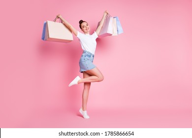 Full length photo of positive cheerful girl enjoy shopping raise many bags wear white t-shirt outfit gumshoes isolated over pastel color background