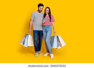 Full length photo of positive couple guy with shopping bags look at smartphone read notification isolated on yellow color background - Powered by Shutterstock