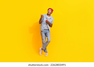 Full length photo of positive excited man wear jeans outfit typing modern gadget thumb empty space isolated yellow color background - Shutterstock ID 2262803491