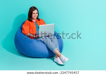 Full length photo of positive girl dressed shirt bean bag writing message device empty space isolated turquoise color background