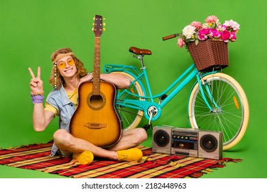 Full Length Photo Of Positive Hippy Guy Sit Plaid Blanket Show V-sign Isolated On Green Color Background