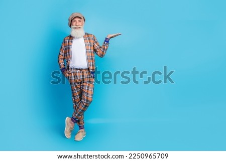 Full length photo of positive man stylish pensioner gentleman wear vintage suit arm present empty space isolated on blue color background