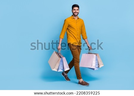 Full length photo of positive person walk hands hold packages isolated on blue color background