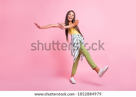 Full length photo of pretty cheerful girl have fun spend holiday wear green pants isolated on shine pink color background
