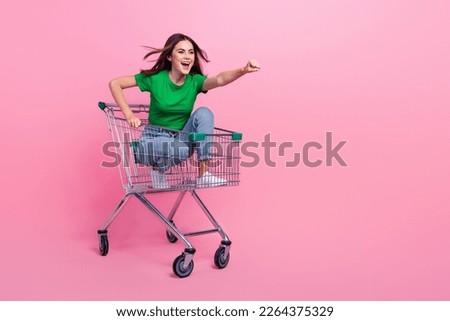 Full length photo of pretty excited lady dressed green t-shirt riding shopping cart empty space isolated pink color background