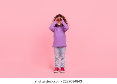 Full length photo of pretty funky little child dressed purple pullover hunting you binoculars isolated pink color background