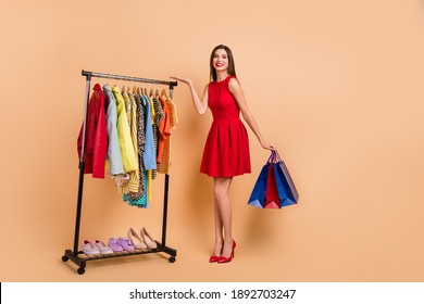 Full length photo of pretty girl hold hand display botique assortment hold bags wear red dress isolated on beige color background