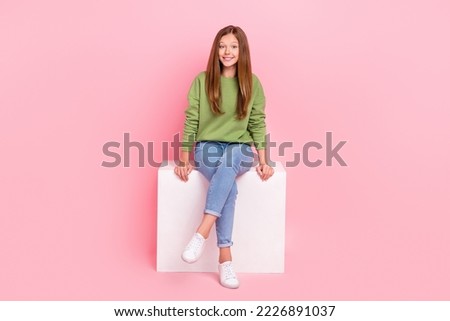 Full length photo of pretty sweet school girl dressed green sweatshirt sitting white cube chair isolated pink color background