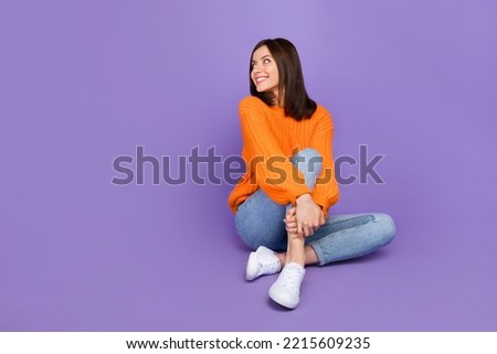 Full length photo of pretty young lady sit floor look empty space dressed stylish orange knitted look isolated on purple color background