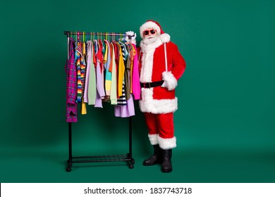 Full length photo of retired grandpa white beard do shopping boutique near hanger weekend sale wear red santa x-mas costume coat gloves sunglass headwear isolated green color background - Powered by Shutterstock