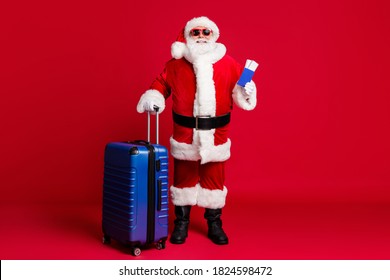 Full Length Photo Of Retired Old Man White Beard Hold Ticket Passport Case Prepare Trip Abroad Wear Santa X-mas Costume Coat Sunglass Headwear Leather Boots Isolated Red Color Background