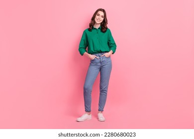 Full length photo of satisfied lovely nice person wear jeans green shirt sneakers standing arms in pockets isolated on pink background