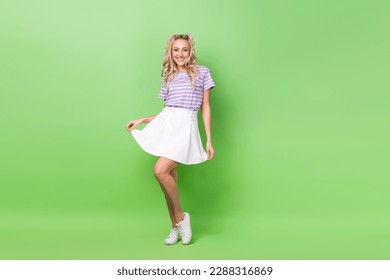 Full length photo of satisfied optimistic girl curly hairdo wear striped t-shirt touching white skirt isolated on green color background