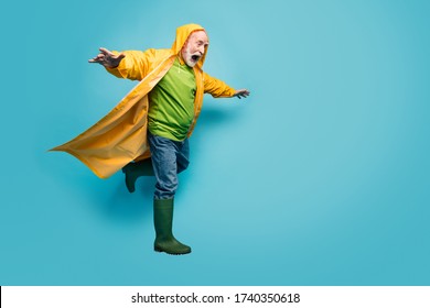 Full Length Photo Of Screaming Grandpa Amazed Walk Street Puddles Rainy Weather Slippery Wet Road Wear Jeans Jumper Gum Boots Yellow Raincoat Isolated Blue Color Background