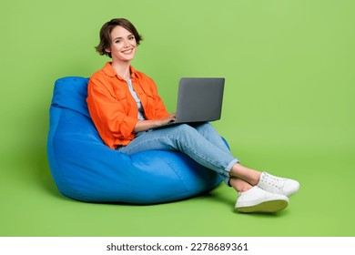 Full length photo of shiny positive lady dressed jeans shirt bean bag working device emtpy space isolated green color background