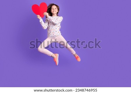 Full length photo of shiny pretty small girl wear dotted sweater jumping rising heart empty space isolated violet color background