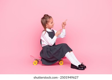 Full length photo of small schoolgirl ride skateboard point look empty space dressed stylish uniform isolated on pink color background - Powered by Shutterstock