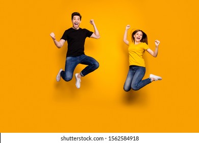 Full length photo of sporty guy and lady couple jumping high active way of life celebrating first win place competition wear casual jeans t-shirts isolated yellow color background
