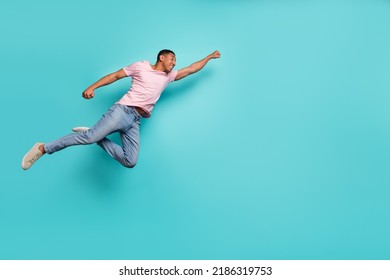Full length photo of strong hurrying guy wear pink t-shirt jumping high flying help empty space isolated teal color background